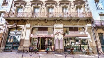 A building with a bakery named 'Meery Cake' on the ground floor, featuring a large window display and outdoor seating.