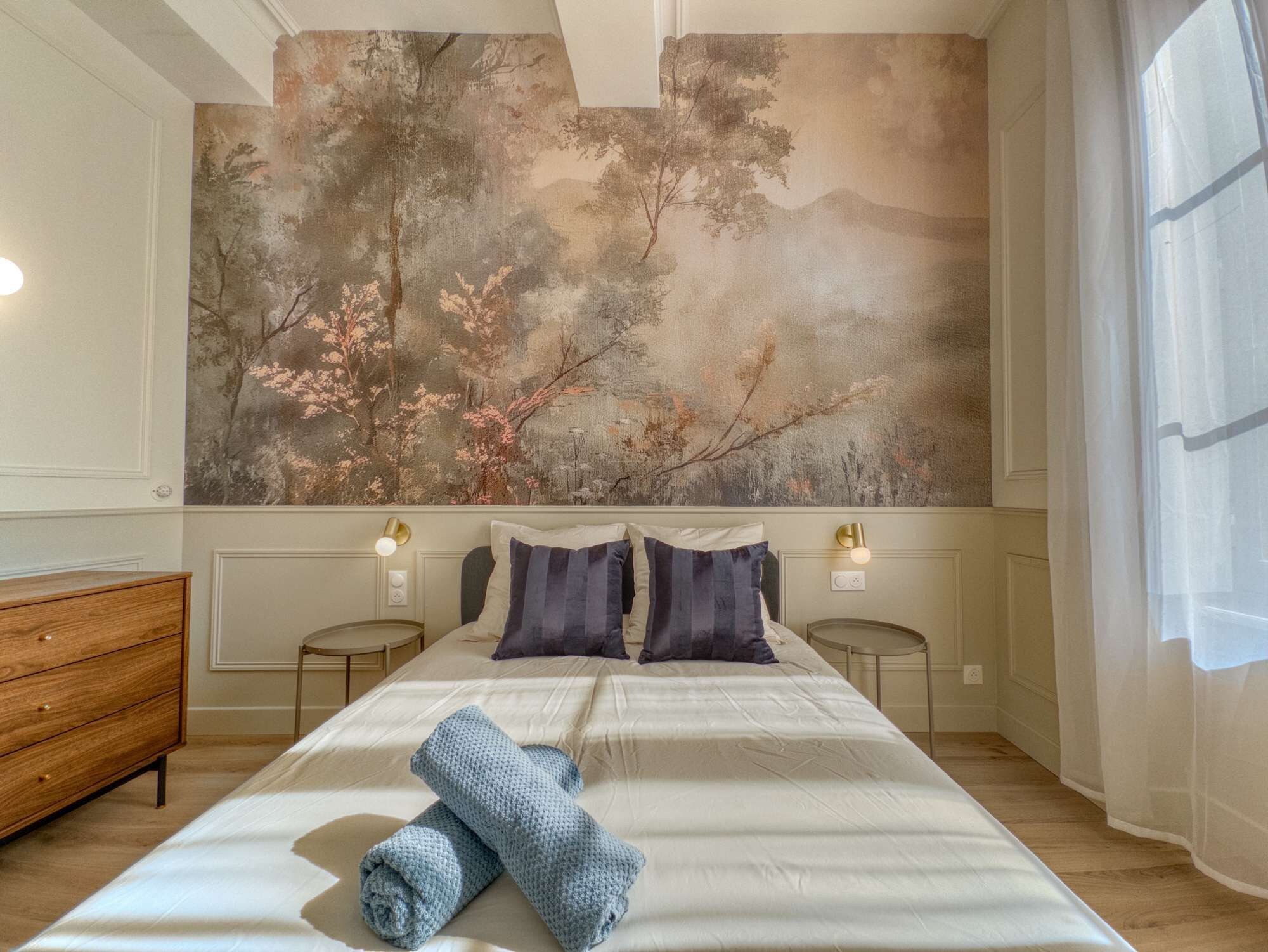 Ett hotellrum med en stor säng, två sängbord, en byrå i trä och en stor väggmålning.