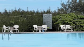 Una piscina amb gandules blanques i una taula, envoltada d'arbres i una zona coberta.