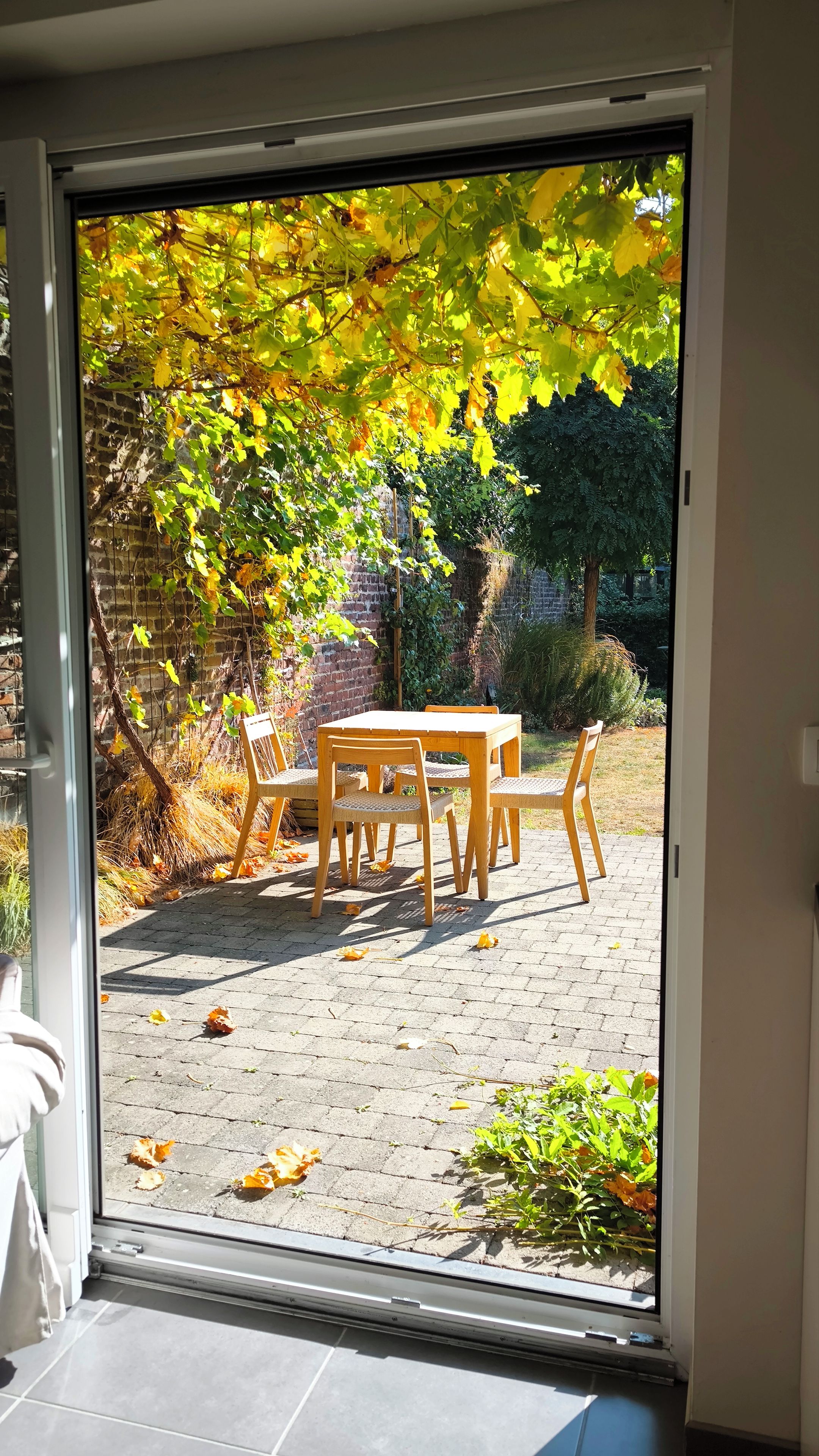 Een terras met een tafel en stoelen, een bakstenen muur en een tuin met bomen.