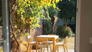 Een terras met een tafel en stoelen, een bakstenen muur en een tuin met bomen.