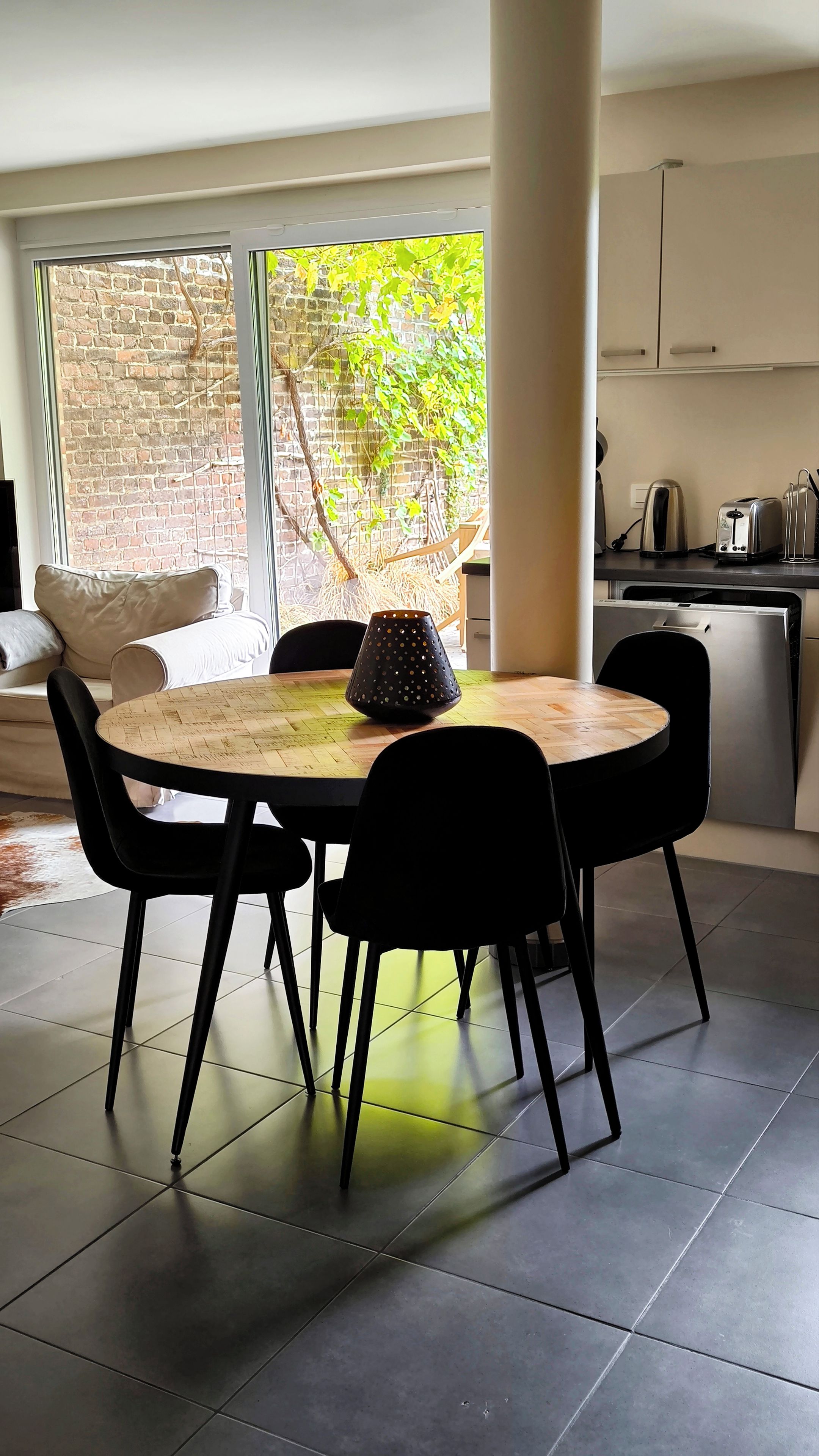 Un comedor moderno con una mesa redonda, sillas negras y una lámpara decorativa.