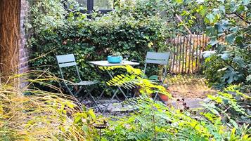 A garden with a table and chairs, surrounded by various plants and trees.