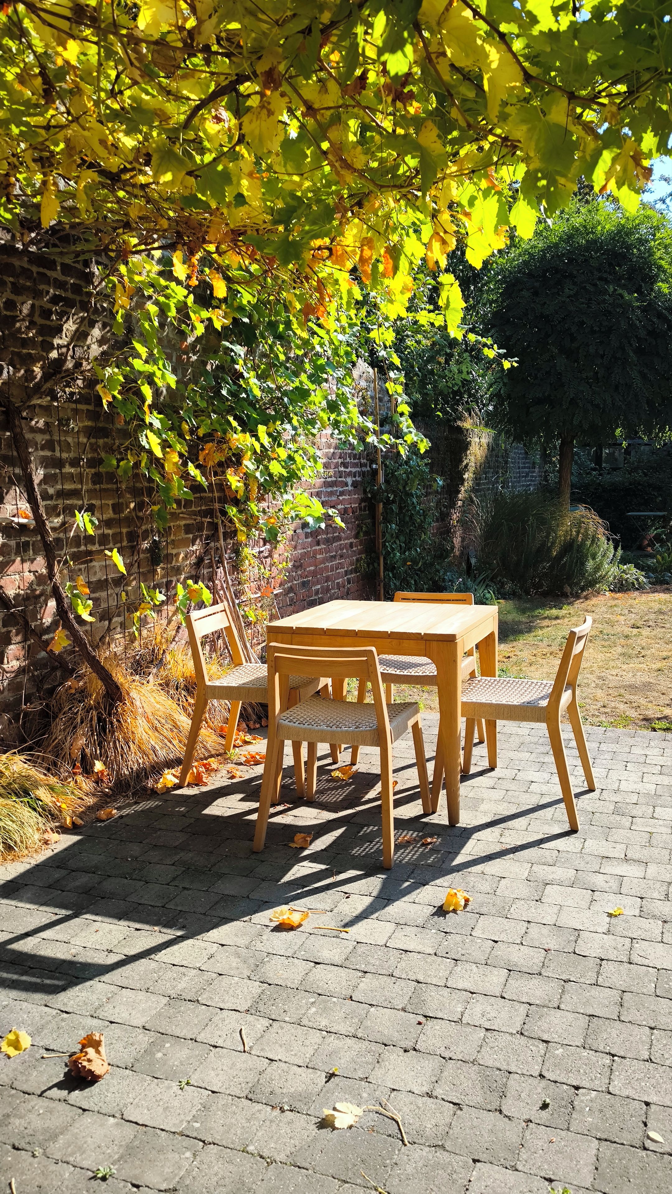 A wooden table and chairs set outdoors, surrounded by a brick wall and foliage.
