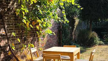 A wooden table and chairs set outdoors, surrounded by a brick wall and foliage.