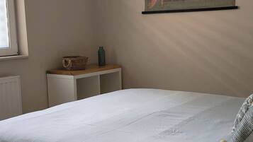 Un dormitorio con una cama, una lámpara colgante, un mapa en la pared y una mesita con una cesta y una botella.