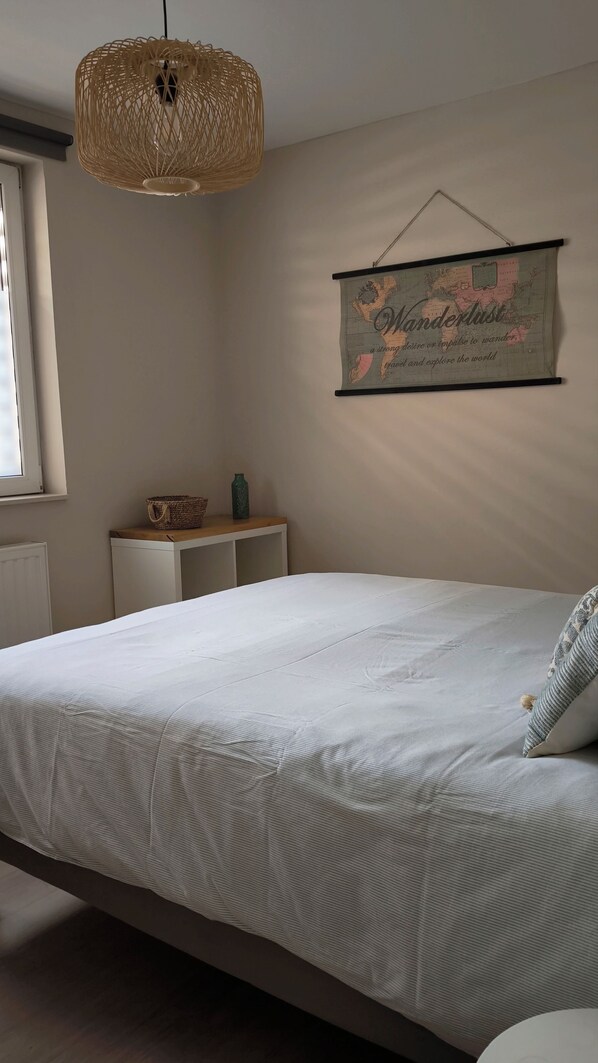 A bedroom with a bed, a hanging light fixture, a map on the wall, and a small table with a basket and a bottle.