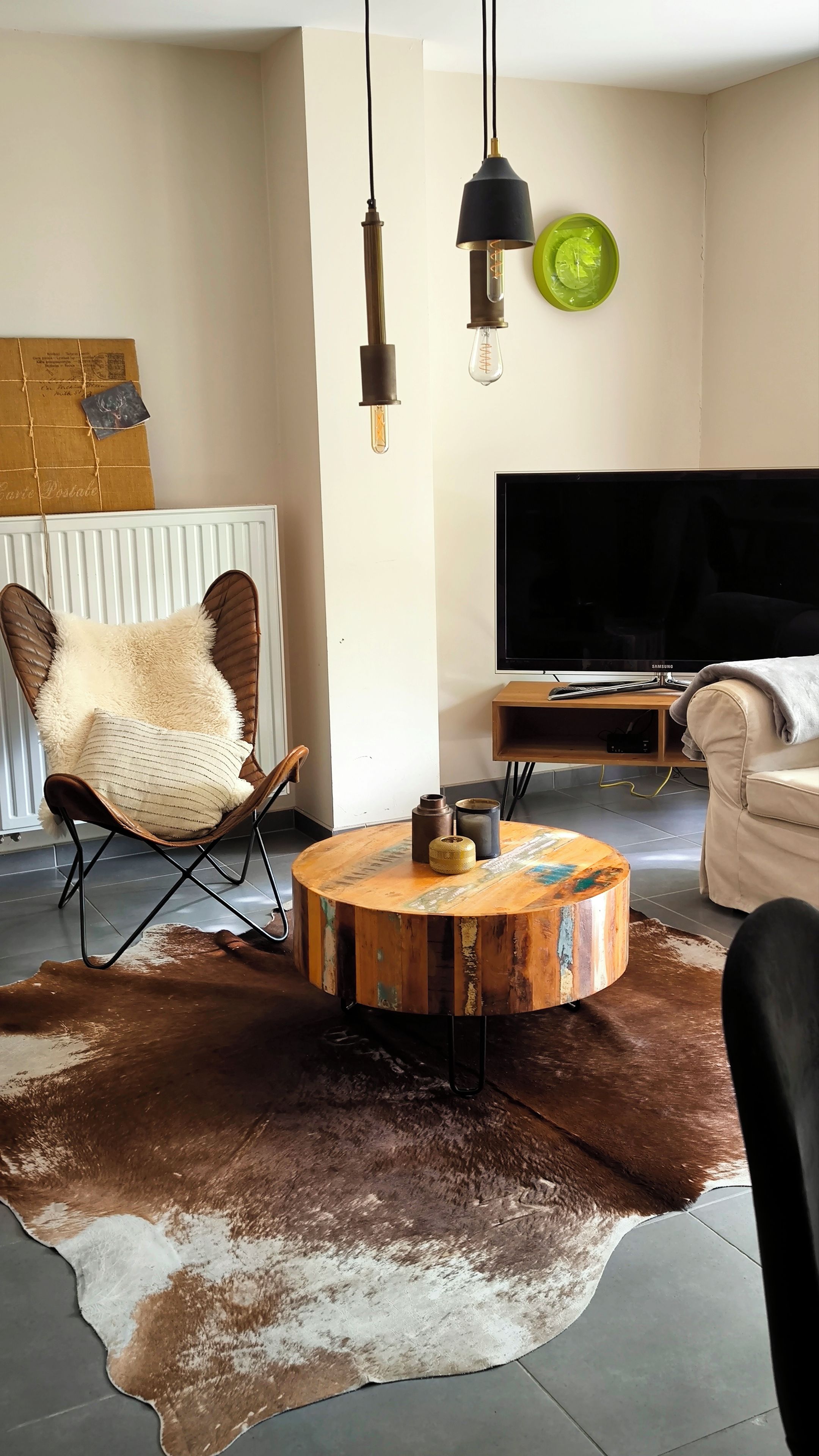 Un salon comprenant une table basse ronde, un canapé en cuir, un téléviseur et un luminaire mural original.