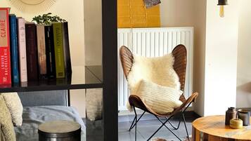Una habitación con estantería, sillón de cuero, mesa redonda de madera, radiador y lámpara colgante.