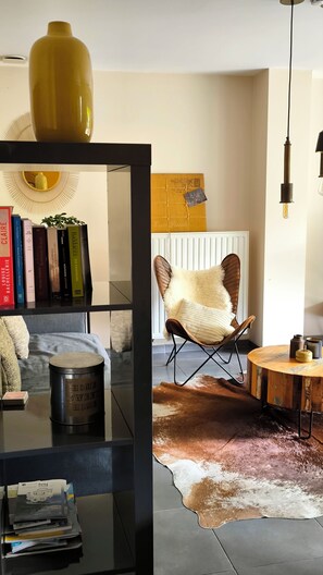 A room with a bookshelf, a leather chair, a round wooden table, a radiator, and a hanging light fixture.