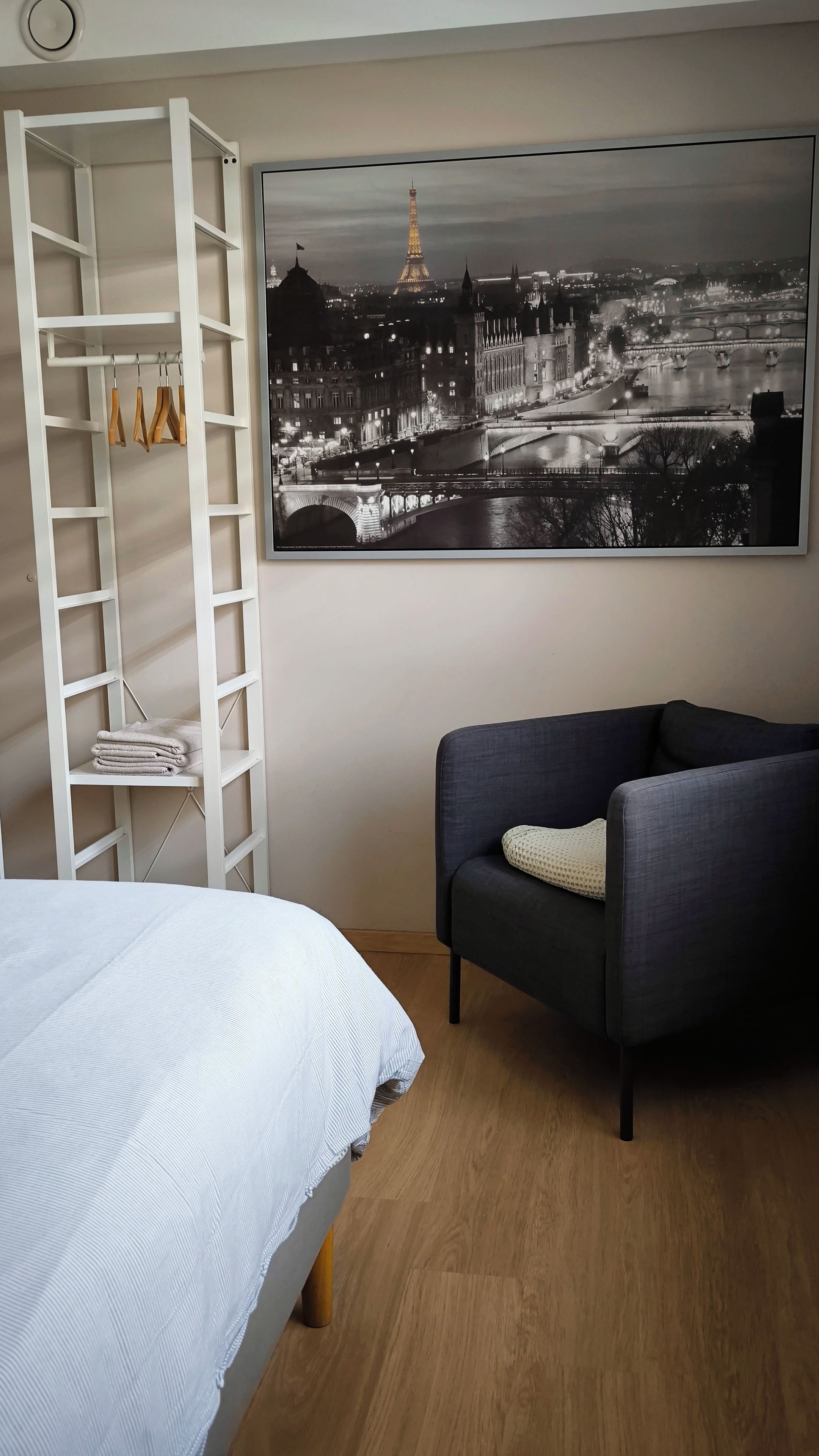 A bedroom with a bed, a wardrobe, a sofa, and a large cityscape painting.