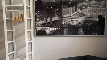 A bedroom with a bed, a wardrobe, a sofa, and a large cityscape painting.