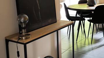 A dining area with a table and chairs, a wall-mounted picture of a deer, a lamp, and a fan on a console table.