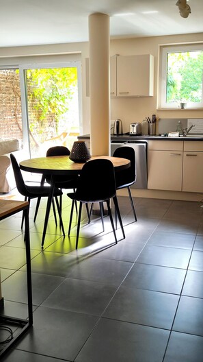 A modern kitchen with a dining area, featuring a round table with chairs, a kettle, and a toaster on the counter.