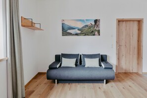 Ein Zimmer mit einer grauen Couch, einer Holztür und einem Landschaftsbild an der Wand.
