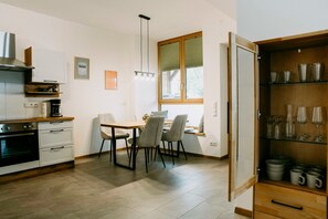 A modern kitchen with a dining area, featuring a stove, oven, and a window with blinds. - Vacation rental with a terrace for up to 4 people (Tuntenhausen)
