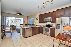 A kitchen with dark wooden cabinets, stainless steel appliances, and a dining area with wicker chairs. - Windsor Palms - 29539 (Kissimmee)