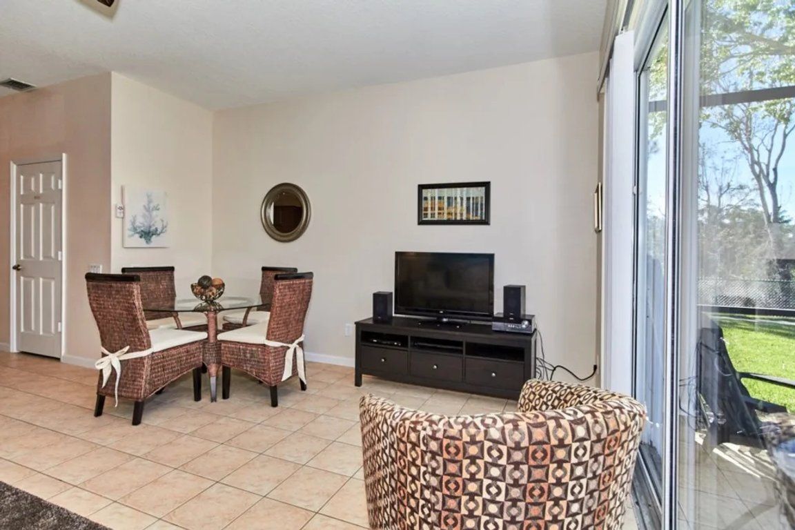 A living room with a dining table, chairs, a television, and a large window.