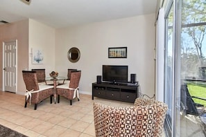 A living room with a dining table, chairs, a television, and a large window. - Windsor Palms - 29539 (Kissimmee)