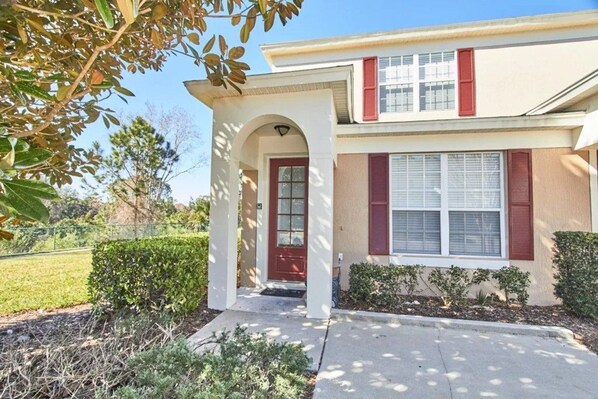 A two-story house with a red door, a covered entryway, and a small front yard with shrubs. - Windsor Palms - 29539 (Kissimmee)