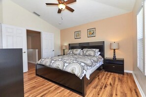 A bedroom with a bed, nightstands, a ceiling fan, and a door. - Windsor Palms - 29539 (Kissimmee)