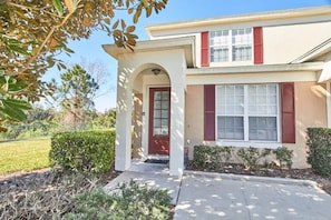A two-story house with a red door, a covered entryway, and a small front yard with shrubs. - Windsor Palms - 29539 (Kissimmee)
