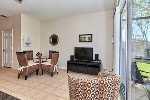 A living room with a dining table, chairs, a television, and a large window. - Windsor Palms - 29539 (Kissimmee)