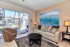 A living room with a sofa, a patterned armchair, a coffee table, and a painting of a wave. - Windsor Palms - 29539 (Kissimmee)