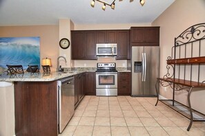 A kitchen with dark wood cabinets, stainless steel appliances, a clock on the wall, and a painting of a wave. - Windsor Palms - 29539 (Kissimmee)