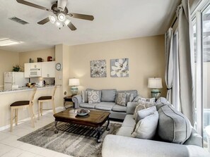 A living room with a sofa, coffee table, and chairs, a kitchen area with appliances, and artwork on the walls. - Windsor Palms - 29543 (Kissimmee)