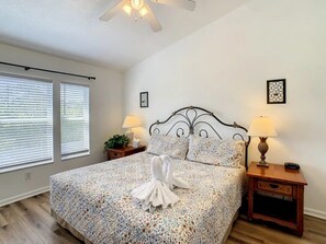 A bedroom with a bed, two bedside lamps, a nightstand, and a window with blinds. - Windsor Palms - 29543 (Kissimmee)