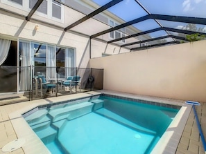 A swimming pool with a glass enclosure, a covered patio area with chairs, and a view of a building with large windows. - Windsor Palms - 29543 (Kissimmee)