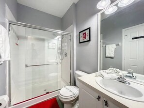 A modern bathroom with a glass-enclosed shower, a white toilet, and a vanity with a sink and mirror. - Windsor Palms - 29551 (Kissimmee)