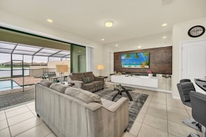 A modern living room with a sofa, a coffee table, and a TV mounted on a wooden wall. - Windsor at Westside - 29923 (Kissimmee)