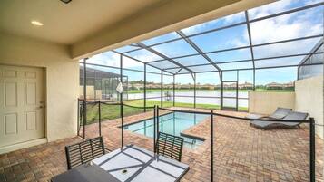 A covered outdoor area with a pool, seating, and a view of the landscape.