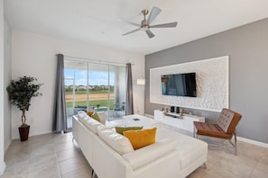 Una sala de estar moderna con un sofá blanco, un sillón marrón, un televisor de pantalla plana montado en una pared texturizada y un ventilador de techo.