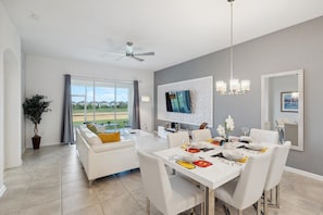 Un comedor moderno con una mesa blanca para cuatro, un ventilador de techo y un amplio ventanal que ofrece vistas al exterior.
