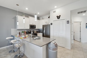 A modern kitchen with white cabinetry, stainless steel appliances, and a central island with bar stools. - Champions Gate - 33029 (Davenport)