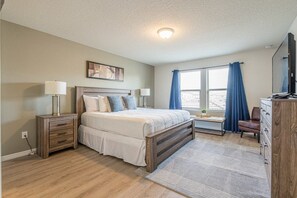 A bedroom with a bed, bedside tables, a dresser, a window with curtains, and a television. - Windsor at Westside - 34484 (Kissimmee)
