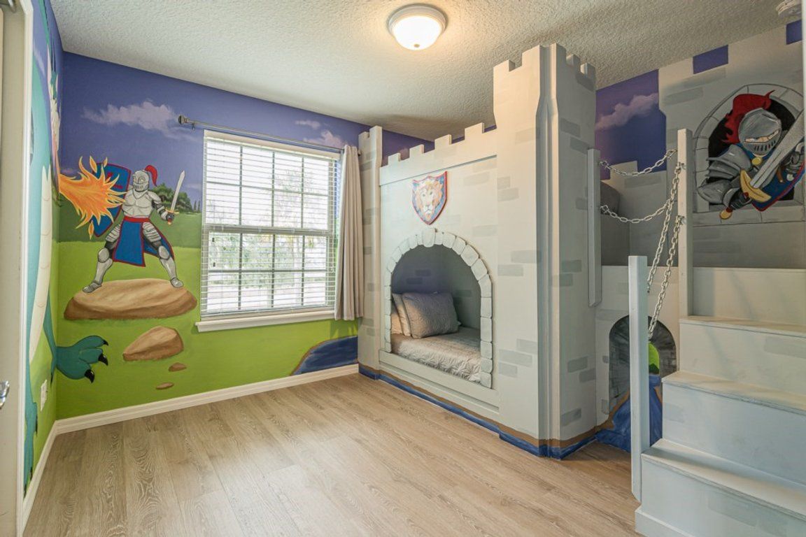 A child's bedroom with a castle-themed mural, a window with blinds, and a bed with a castle-like headboard.
