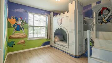 A child's bedroom with a castle-themed mural, a window with blinds, and a bed with a castle-like headboard.