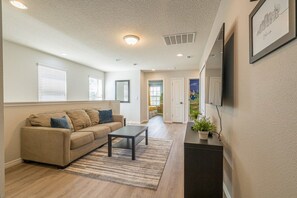 A living room with a sofa, a coffee table, and a TV mounted on the wall. - Windsor at Westside - 34484 (Kissimmee)