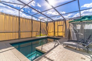 A swimming pool with a clear blue water surface, surrounded by a brick patio and a covered area with a metal frame and beige curtains. - Windsor Island - 34516 (Davenport)