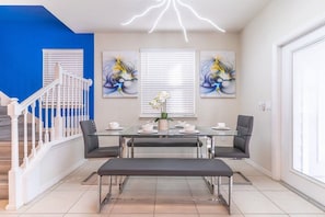 A dining area with a glass table, four chairs, a bench, and two wall-mounted paintings. - Windsor Island - 34516 (Davenport)