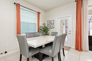 Un coin repas comprenant une table en marbre et quatre chaises rembourrées, une plante en pot et une porte avec une fenêtre.