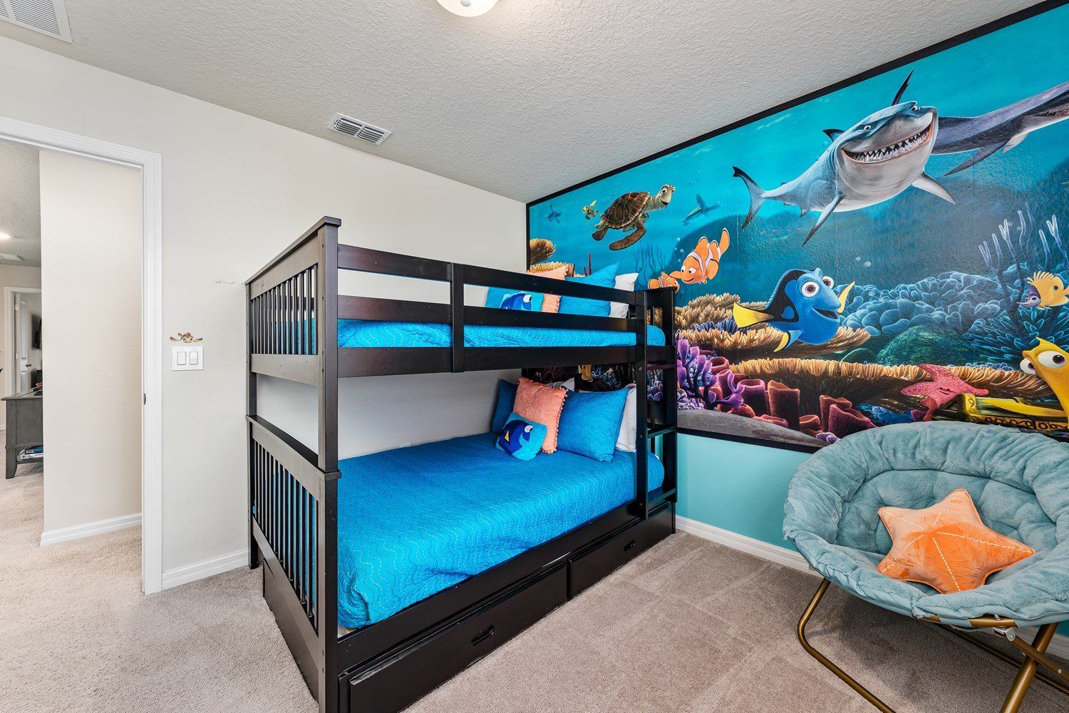 Un lit superposé avec un matelas bleu, une fresque murale représentant des créatures marines, et une chaise avec un coussin.