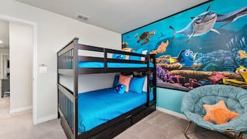 Un lit superposé avec un matelas bleu, une fresque murale représentant des créatures marines, et une chaise avec un coussin.