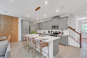 A modern kitchen with grey cabinets, a central island with bar stools, and a staircase with wooden railings. - Solara Resort - 34550 (Kissimmee)