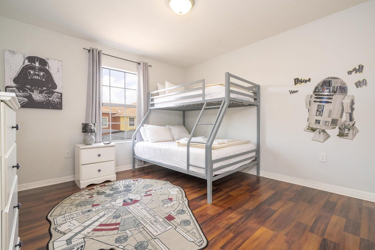 A bunk bed room with a Star Wars themed wall, a window with curtains, a bedside table, and a Star Wars themed rug.