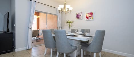 A dining area with a white table, grey chairs, and a chandelier.